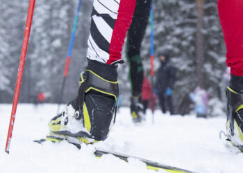 Smiling baby carrying vibrant ski helmet holds junior skis in the front of High Country Ski & Tennis and wintry weather sports keep entrance